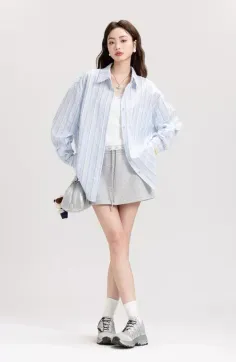 Woman with long hair wearing a striped shirt and grey shorts on a white background