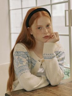 Young woman with red hair and freckles wearing a cardigan, resting her chin on her hand