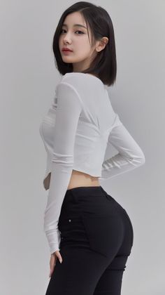 Woman with short black hair in a white crop top and black pants posing indoors