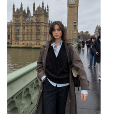 Woman in a trench coat and sweater on a wet bridge with a cityscape in the background