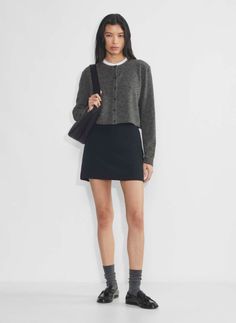 Woman in a gray cropped cardigan and black mini skirt with a shoulder bag