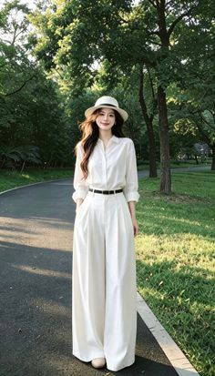 Woman in a white shirt and wide-leg pants with a hat in a park