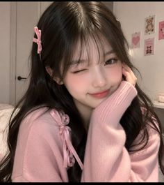 Girl with long dark hair wearing a pink sweater and winking