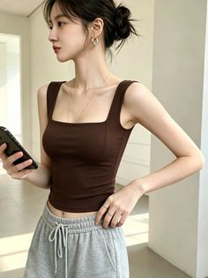 Woman in a brown tank top and grey sweatpants holding a phone indoors