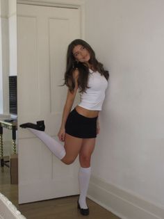 Woman in a white tank top and black mini skirt posing indoors