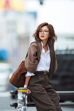 Woman with short hair and glasses wearing a brown cardigan and white shirt outdoors
