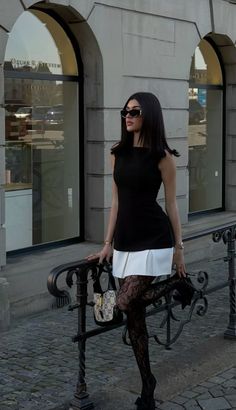 Woman in a black top, white skirt, and lace stockings posing outdoors