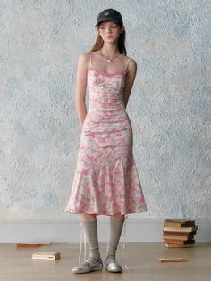 Young woman in a pink floral dress and baseball cap standing indoors