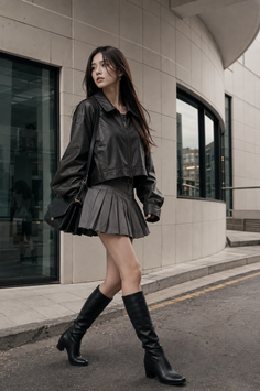 Woman in a leather jacket and pleated skirt walking on an urban street