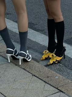 Two people standing on a street, one wearing high heels and the other wearing yellow shoes