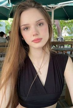 Young woman with long hair wearing a black top and necklace outdoors