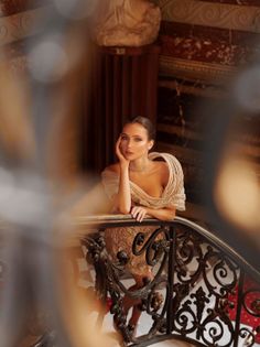 Woman in an elegant evening dress leaning on an ornate railing indoors
