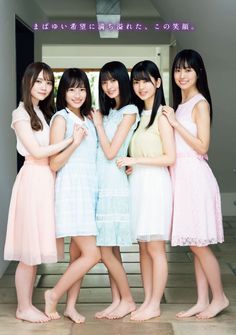 Five young women in pastel dresses standing barefoot indoors
