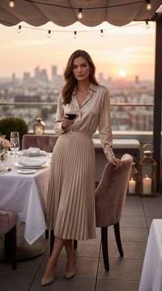 Woman in an elegant outfit holding a wine glass on a rooftop at sunset