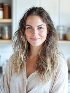 Woman with long wavy hair and a casual shirt smiling indoors