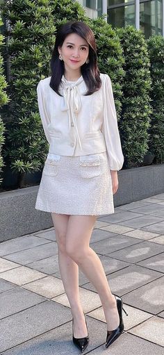 Woman in a white tweed skirt suit and black heels standing outdoors