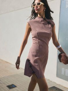 Woman in a gingham dress and sunglasses walking outdoors in daylight