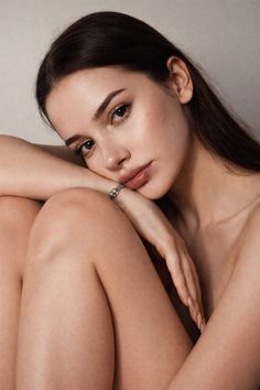 Woman with long dark hair and natural makeup, posing with exposed skin