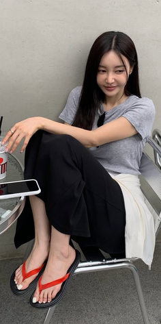 Woman with long black hair sitting outdoors in a gray t-shirt and black pants