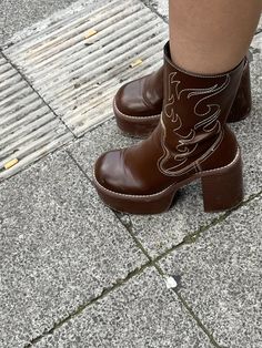 Person wearing brown platform cowboy boots with white stitching on a concrete ground