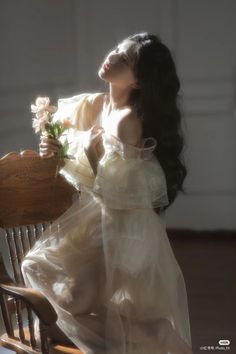 Woman in a sheer dress holding flowers, bathed in soft light