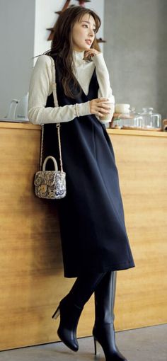 Woman in a black dress and white turtleneck holding a cup indoors