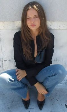 Woman with long hair winking while sitting outdoors in a black shirt and jeans