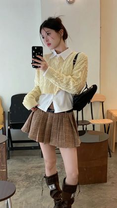 Woman in a plaid skirt and cropped cardigan taking a mirror selfie