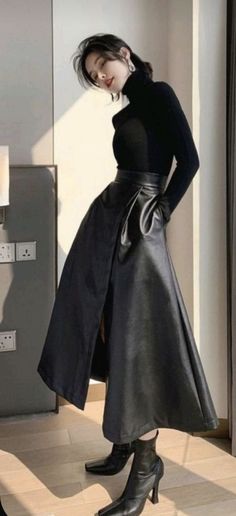 Woman in a black turtleneck and leather skirt posing indoors with soft lighting
