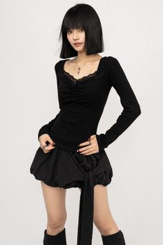Woman with a black bob and bangs wearing a black top and mini skirt