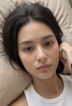 Woman with dark hair in a white tank top lying on a pillow