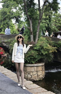 Woman in a straw hat and white skirt posing by a river with green trees