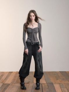 Woman with long hair wearing a gray top and wide leg pants on a wooden floor