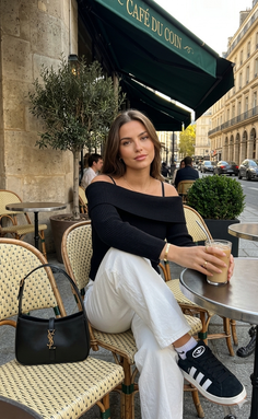 Woman with long hair in an off-shoulder top and white pants at an outdoor cafe
