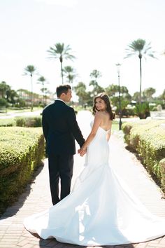Couple in wedding attire holding hands and walking outdoors with palm trees