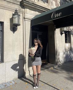 Woman in a houndstooth skirt and sunglasses holding flowers on a sunny street