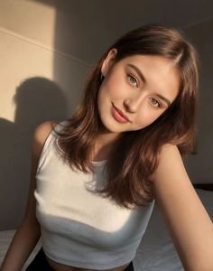 Woman with brown hair and green eyes in a white tank top indoors with soft lighting