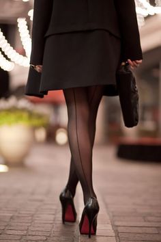 Woman in a black dress and seamed stockings walking away at night