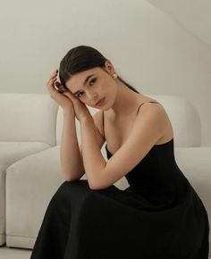 Woman in a black dress with long hair, leaning on her hands indoors