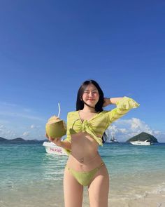 Woman in a green bikini and sheer top holding a coconut on a beach