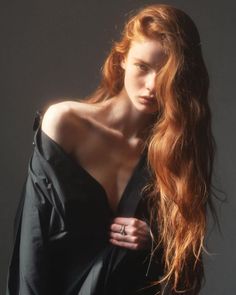 Woman with long red hair wearing an unbuttoned black shirt with exposed skin