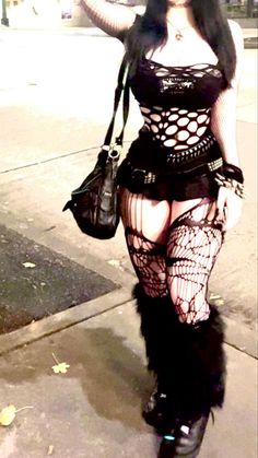 Woman in gothic attire with fishnet top and stockings outdoors at night