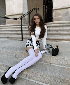 Woman with long hair wearing a crop top and mini skirt sitting on stone steps