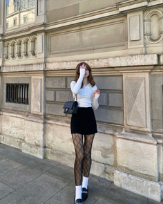 Woman in a black mini skirt and patterned tights standing outdoors