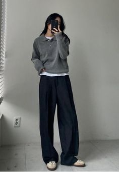 Woman in a gray sweater and wide leg pants taking a mirror selfie
