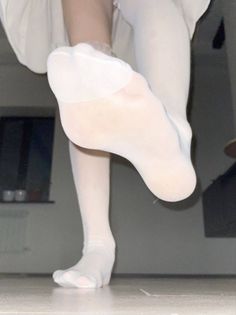 Person wearing white stockings, with one foot raised, viewed from a low angle