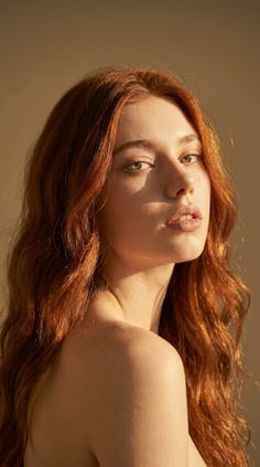 Woman with long red hair and green eyes, exposed shoulders, looking over her shoulder