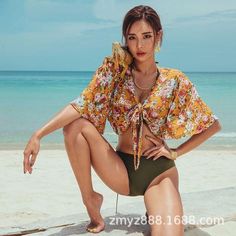 Woman in a floral top and bikini bottoms posing on a beach