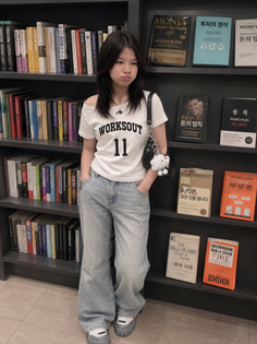 Young woman in a white t-shirt and loose jeans standing in front of a bookshelf