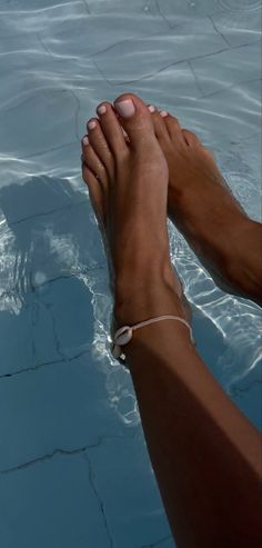 Feet with light pink pedicure and a shell anklet in a swimming pool